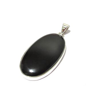 May include: A polished black oval pendant with a silver-colored bail. The pendant has a smooth, glossy surface and a silver-colored border. The pendant is set against a white background. This jewelry item is suitable for everyday wear.