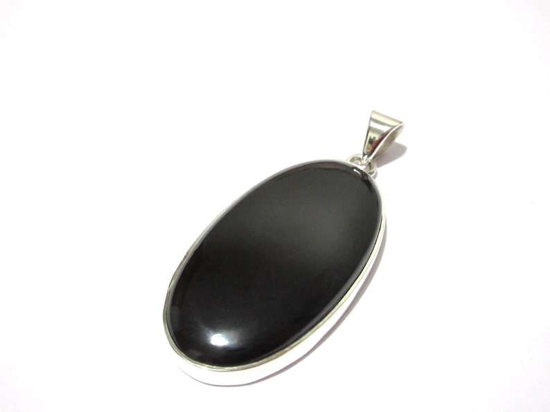 May include: A polished black oval pendant with a silver-colored bail. The pendant has a smooth, glossy surface and a silver-colored border. The pendant is set against a white background. This jewelry item is suitable for everyday wear.