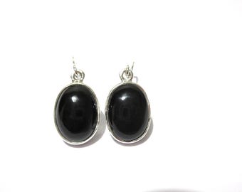 May include: A pair of oval-shaped earrings featuring smooth, polished black stones set in silver-toned metal frames. Each earring includes a small silver jump ring at the top for attachment, showcasing a simple, symmetrical design with a glossy finish.