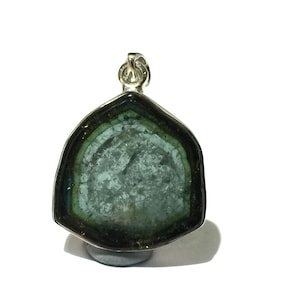 Può includere: Ciondolo con pietra preziosa con bague d'argento. Il ciondolo presenta una fetta di tormalina con un bordo esterno verde scuro, una fascia verde più chiara e un centro verde pallido. La pietra è incastonata in una lunetta d'argento.