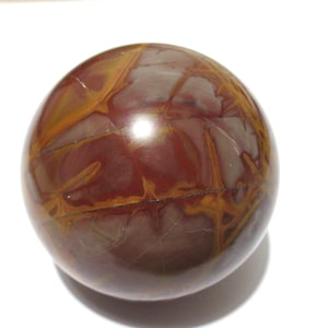 May include: A polished, spherical stone with a rich, earthy color palette. The orb features a blend of deep burgundy and warm golden-brown hues, with intricate veining patterns across its surface. The stone's smooth, reflective finish suggests it is a decorative item.