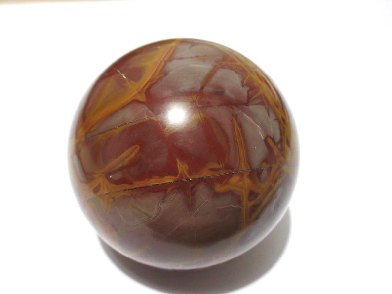 May include: A polished, spherical stone with a rich, earthy color palette. The orb features a blend of deep burgundy and warm golden-brown hues, with intricate veining patterns across its surface. The stone's smooth, reflective finish suggests it is a decorative item.