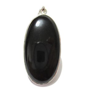 May include: A polished black oval pendant with a silver-colored metal border and a small loop at the top for a chain. The pendant is set against a white background.