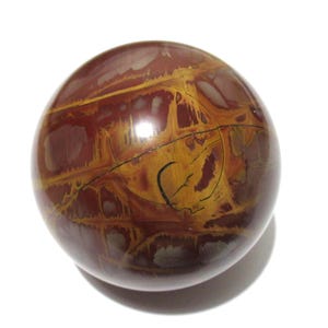 May include: A polished, spherical stone with a mix of reddish-brown and golden-yellow hues. The orb-shaped object has a glossy finish and intricate patterns, suggesting a natural mineral specimen. The stone sits on a white background.