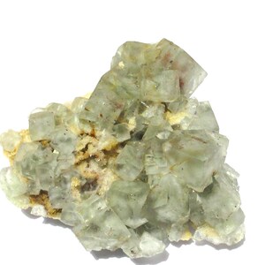 May include: A cluster of translucent, pale green fluorite crystals. The crystals have a cubic structure and are clustered together on a matrix of beige and brown minerals. The overall appearance is crystalline and natural.