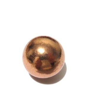 May include: A single spherical object with a smooth, polished copper-coloured metallic surface. The sphere features a reflective finish that catches light, creating bright highlights across its rounded, uniform shape against a plain white background.