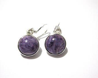 May include: A pair of round earrings featuring polished purple charoite cabochons set in silver-toned metal bezels. Each earring includes a simple silver-toned hook wire for attachment, showcasing the natural swirling patterns of the stone.
