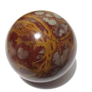 May include: A polished, spherical gemstone with a rich, reddish-brown base color. The stone features intricate patterns of golden-yellow veins and lighter, off-white inclusions, creating a unique and natural design. The sphere is smooth and reflective.