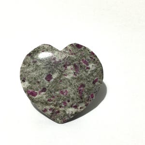 以下が含まれることがあります： ピンクと赤の斑点模様が特徴的な、グレーを基調としたハート型の石。滑らかで光沢のある表面で、装飾品やジュエリーとして使用される可能性があります。滑らかでわずかに光沢のある仕上がりです。
