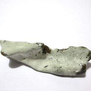 May include: A handcrafted, organic-shaped ceramic piece with a light green glaze and dark brown edges. The surface has a textured appearance with small holes, suggesting a natural, earthy aesthetic. The object is likely a decorative item.