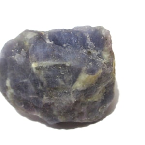 May include: A raw, unpolished mineral specimen featuring a mix of deep violet and light lavender hues with visible white and cream-colored inclusions. The stone has an irregular, jagged shape with a textured, crystalline surface throughout.