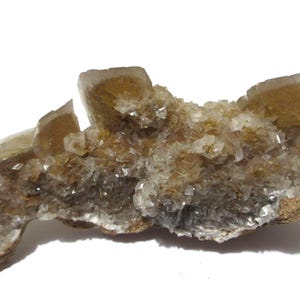 May include: A cluster of light brown and clear crystal formations. The crystals have a rough, textured appearance and are clustered together on a brown base. The crystals are in various sizes and shapes, with some appearing more rectangular.