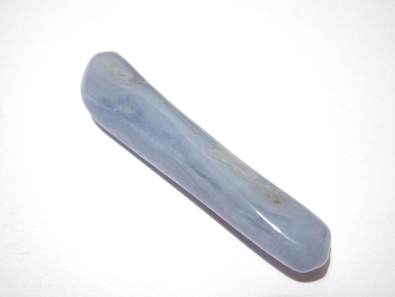 May include: A smooth, elongated blue lace agate crystal wand. The wand is a pale blue color with subtle white and gray marbling. The crystal is polished and has rounded ends. The wand is approximately 6 inches long.