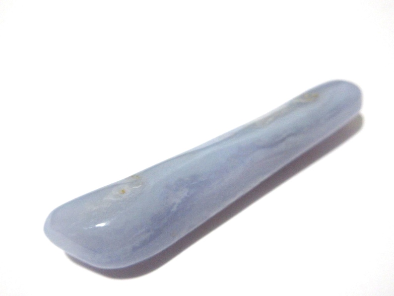 May include: A smooth, elongated blue lace agate gemstone. The polished stone has a rounded shape and a pale blue color with subtle white and tan marbling. The gemstone is approximately 4 inches long.