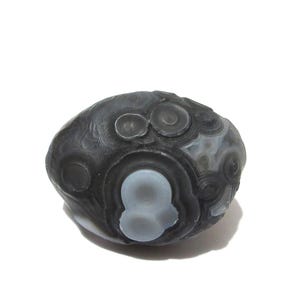 May include: A polished, rounded stone featuring a dark charcoal gray and black base color with distinct, lighter gray circular and eye-like banding patterns across its surface. The stone has a smooth, organic shape with a glossy, reflective finish.