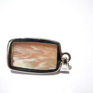 Pu&ograve; includere: Un ciondolo rettangolare con una cornice color argento. Il ciondolo presenta una pietra color pesca chiaro con un motivo fibroso. L'anello &egrave; un piccolo anello attaccato alla parte superiore della cornice. Il ciondolo &egrave; su sfondo bianco.