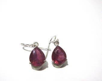 May include: A pair of teardrop-shaped earrings featuring faceted deep pink stones set in silver-toned metal. Each earring hangs from a curved silver-toned hook, showcasing a polished finish and a clear, vibrant color profile for the stones.