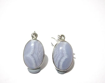 May include: A pair of oval-shaped earrings featuring pale blue gemstones with white veining, set in silver-colored metal. The earrings are displayed against a white background, showcasing their delicate design and color.