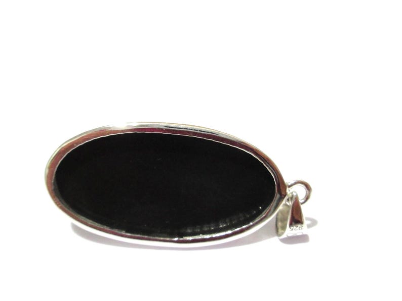 May include: Oval-shaped pendant with a polished black stone set in a silver-colored metal frame. The pendant has a loop for a chain and is set against a white background. The jewelry piece is a simple, elegant design.