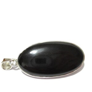 May include: A black oval pendant with a silver-colored metal border and bail. The pendant has a smooth, polished surface and is set against a white background. The pendant is approximately 1.5 inches long.