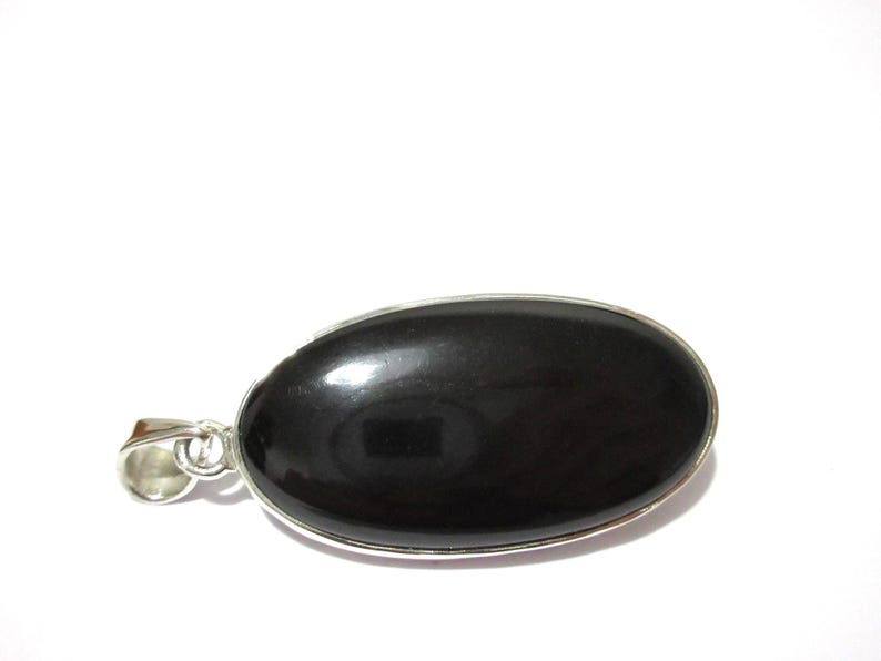 May include: A black oval pendant with a silver-colored metal border and bail. The pendant has a smooth, polished surface and is set against a white background. The pendant is approximately 1.5 inches long.