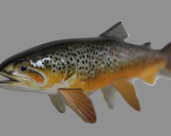 Könnte beinhalten: Ein brauner Bachforellenfisch mit schwarzen Flecken und einem gelben Bauch. Der Fisch ist eine realistische Nachbildung und aus Keramik.