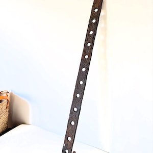 May include: A rusty metal hook with a long, thin shaft and a curved hook at the end. The shaft has a series of evenly spaced holes along its length.