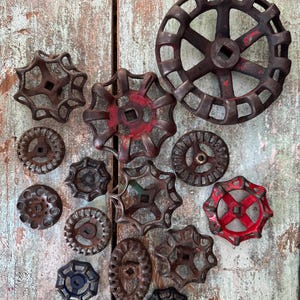 May include: A collection of antique, cast iron valve handles in various shapes and sizes. The handles are primarily shades of brown with hints of red paint, arranged on a weathered, distressed wooden surface. These vintage industrial pieces offer a rustic aesthetic.