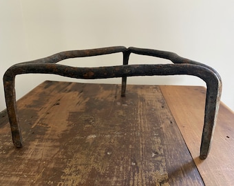 May include: A rustic, iron tripod stand with a simple, curved design. The stand is made of dark metal and has a weathered, aged appearance.