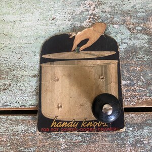 May include: Vintage black and white cardboard tag with a hand holding a pot lid. The tag reads "handy knobs for pot covers - doors - drawers".