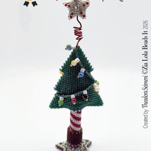 May include: A beaded Christmas tree ornament featuring a green triangular tree with multi-coloured bead lights, a red and white striped trunk, and a star topper. The text reads: Christmas with a 2 and a on A atop a. Created by Theodora Seimeni ©Zia Lola Beads It 2026.