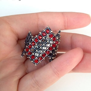 May include: A red and silver beaded ring with the text "Queen of Diamonds ring" above the ring.