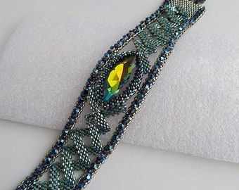 May include: A beaded bracelet with a green and blue color gradient. The bracelet features a large, faceted, green crystal in the center. The bracelet is made with small, silver beads and has a silver clasp. The text "Avalon bracelet" is visible in the top left corner of the image.