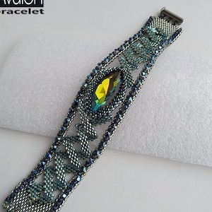 Op de afbeelding: Een kralenarmband met een kleurverloop van groen naar blauw. De armband heeft een grote, gefacetteerde, groene kristal in het midden. De armband is gemaakt van kleine, zilveren kralen en heeft een zilveren sluiting. De tekst "Avalon bracelet" is zichtbaar in de linkerbovenhoek van de afbeelding.