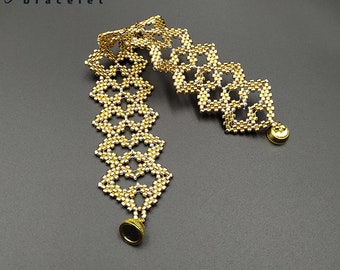 Peut inclure: Un bracelet en perles dorées avec un design délicat et complexe. Le bracelet est fait de petites perles rondes et présente un motif carré. Le bracelet est terminé par deux fermoirs dorés.