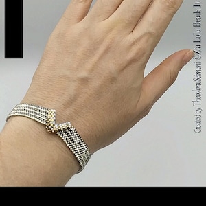 Könnte beinhalten: Ein silbernes und goldenes Perlenarmband mit einem V-förmigen Design. Das Armband befindet sich an einem Handgelenk.