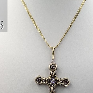 Könnte beinhalten: Eine goldene Kettenkette mit einem Perlenkreuzanhänger. Das Kreuz besteht aus kleinen, dunkelvioletten Perlen und hat einen klaren Kristall in der Mitte. Die Kette liegt auf einem weißen Hintergrund.