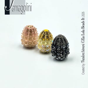 May include: Three beaded egg-shaped ornaments in soft pink, yellow, and dark gray. The ornaments are covered in small beads, creating a textured surface. The image includes the text "Jamagolini" and "Created by Theodora Seimeni ©Zia Lola Beads It 2026".