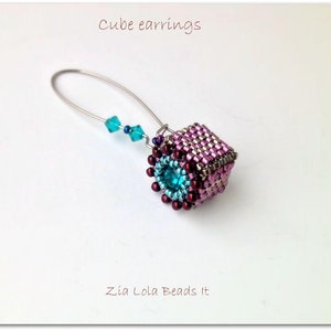May include: A pair of cube earrings with a pink, purple, and silver beaded design. The earrings feature a turquoise blue gemstone in the center of each cube. The earrings are hanging from silver wire.