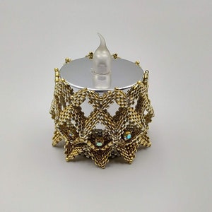 May include: A decorative candle holder with a gold beaded exterior. The holder has a silver base and a clear, flame-shaped LED light. The beaded design features a geometric pattern with iridescent accents, creating a unique and elegant look.