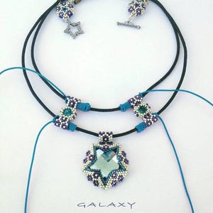 May include: A beaded necklace with a star-shaped pendant featuring a clear crystal. The necklace is made with black cord and purple and white beads. The pendant is surrounded by a beaded border. The necklace has a toggle clasp.