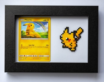 Puede incluir: Dos cartas de Pokémon enmarcadas con arte pixelado de Pikachu y Eevee. Las cartas son del set Básico y presentan los nombres y las estadísticas de los Pokémon. El arte pixelado está hecho de pequeñas cuentas de colores.