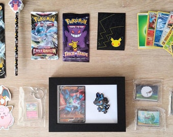 Puede incluir: Una colección de artículos del juego de cartas coleccionables Pokémon, que incluye cartas, pegatinas, un lápiz y obras de arte enmarcadas. Las cartas presentan varios personajes Pokémon, y las pegatinas incluyen figuras populares. Los artículos están dispuestos sobre una superficie de madera clara.