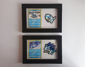 Puede incluir: Dos marcos de fotos negros con paspartús blancos, cada uno contiene una carta de Pokémon y una representación de pixel art del Pokémon. El marco superior presenta una carta de Sandshrew y un Sandshrew de pixel art azul. El marco inferior presenta una carta de Sandslash y un Sandslash de pixel art azul.