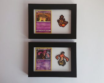 Puede incluir: Dos marcos de fotos negros con paspartús blancos. Cada marco contiene una carta de Pokémon y una representación de pixel art del Pokémon. El marco superior presenta una carta morada y amarilla con el Pokémon 'Parasect' y una figura de pixel art marrón. El marco inferior presenta una carta morada y amarilla con el Pokémon 'Gourgeist' y una figura de pixel art naranja.