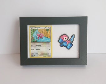 Puede incluir: Una carta de Pokemon enmarcada con Porygon, un Pokemon digital rosa y azul. La carta está rodeada por un marco negro y una versión de arte de píxeles de Porygon se muestra junto a la carta.