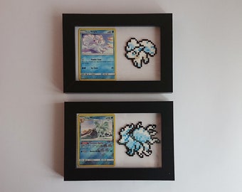 Puede incluir: Dos marcos de fotos negros con paspartús blancos. Cada marco contiene una carta de Pokémon y una representación de pixel art del Pokémon. El marco superior presenta una carta de Alolan Vulpix con el texto "Alolan Vulpix #181" y una representación de pixel art de Alolan Vulpix. El marco inferior presenta una carta de Alolan Ninetales con el texto "Alolan Ninetales #182" y una representación de pixel art de Alolan Ninetales.