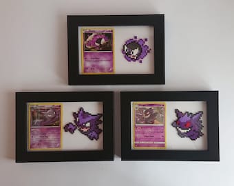 Puede incluir: Tres marcos de fotos negros con paspartús blancos, cada uno contiene una carta de Pokémon y una representación de pixel art del Pokémon. Los Pokémon que aparecen son Gengar, Haunter, y una carta de evolución de Gengar.