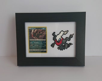 Puede incluir: Obra de arte enmarcada con una carta Pokémon Darkrai y un Darkrai de pixel art. La carta tiene un fondo verde y amarillo con el nombre "Darkrai" en la parte superior. El pixel art es negro, blanco y rojo.