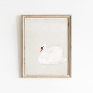Vintage swan painting in a distressed pale wood frame, featuring a softly painted white swan with a black face and bright orange beak resting against a lightly textured cream background.